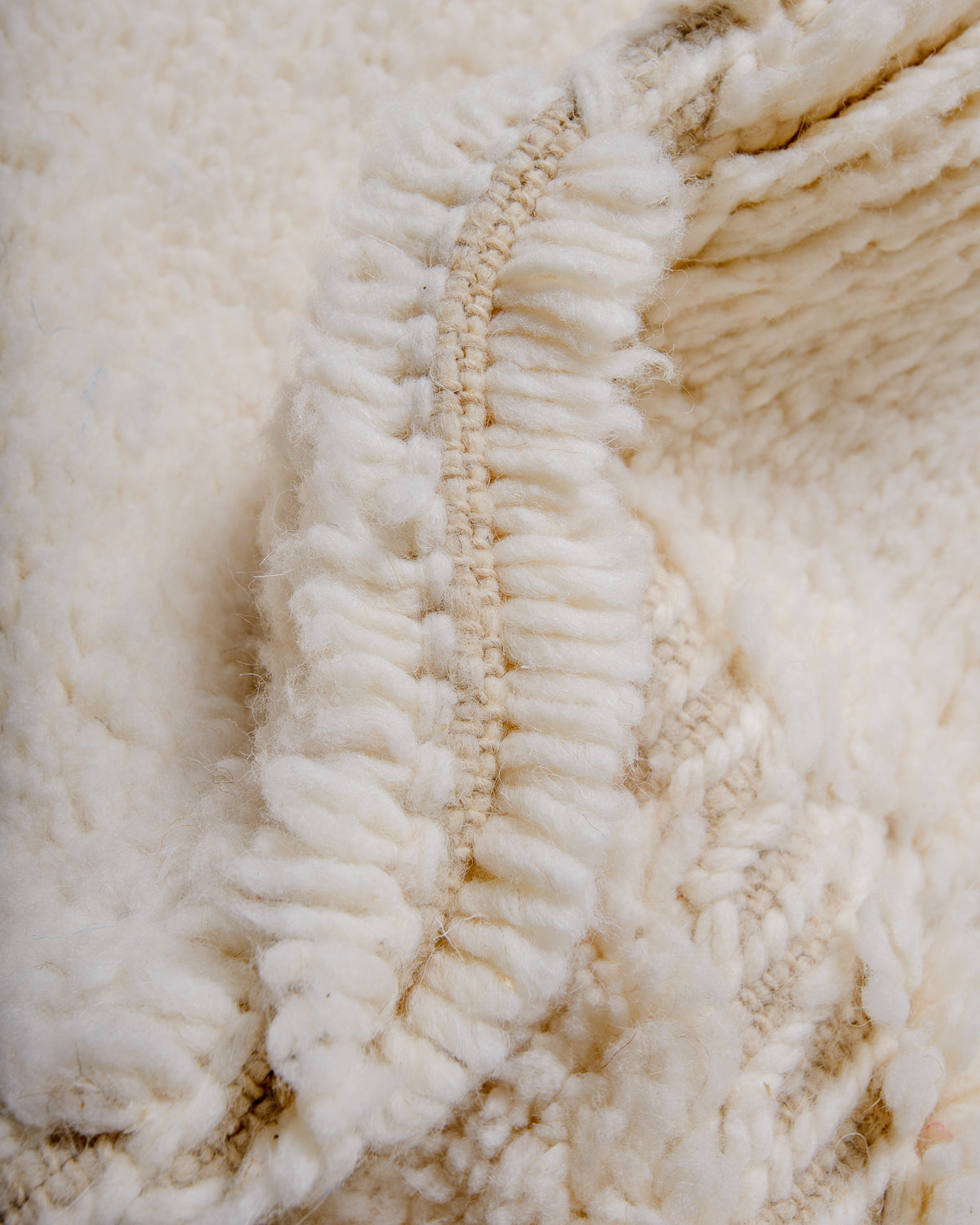Detail of fluffy cream Berber rug showing the wool pile and number of knots in each row.